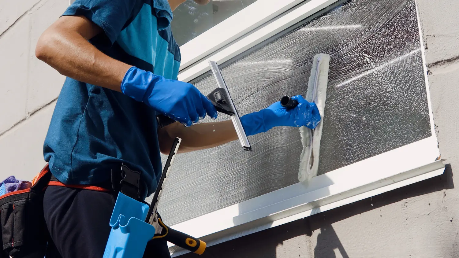 Männliche Reinigungskraft in Latzhose reinigt die Fenster und Schaufenster eines Geschäfts mit Spezialgeräten